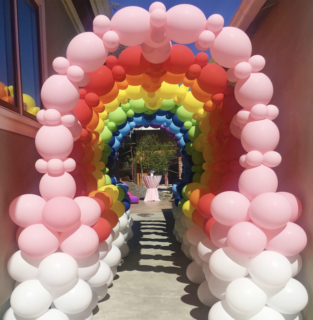 A walkway with balloons and a rainbow arch.