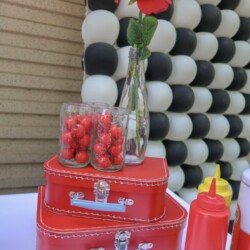 A table with red and white balloons, a vase of flowers and three red suitcases.