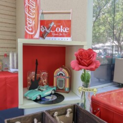A red rose in a glass vase on top of a shelf.