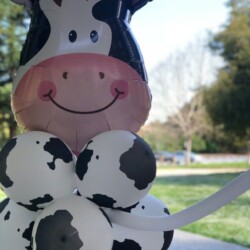 A cow balloon animal is standing in the grass.
