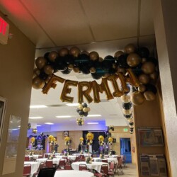 A room with many tables and chairs, balloons hanging from the ceiling.