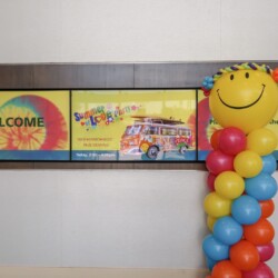 A smiley face balloon column in front of a welcome sign.