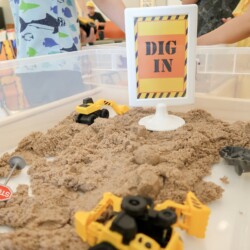 A table with sand and toy trucks in it.