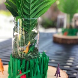 A vase with green grass and some toy dinosaurs in it