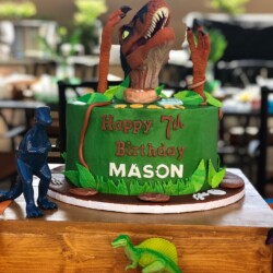 A green cake with dinosaur decorations on top of it.
