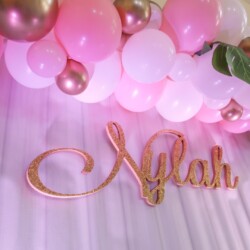 A pink balloon arch with balloons and a name sign.