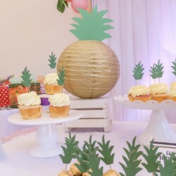 A table with cupcakes and paper pineapple decorations.