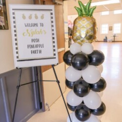 A pineapple balloon tower with balloons and a sign.
