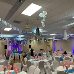 A banquet hall with tables and chairs, balloons hanging from the ceiling.