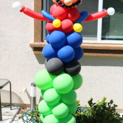 A balloon sculpture of mario is standing on top of balloons.