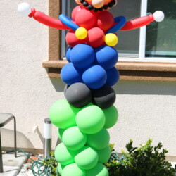 A balloon sculpture of mario is standing on top of balloons.