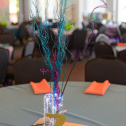 A table with orange napkins and purple flowers in it.