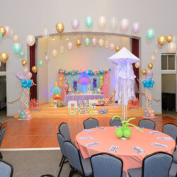A room with tables and chairs, balloons and lights.