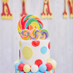 A cake with lollipops and balloons on top of it.