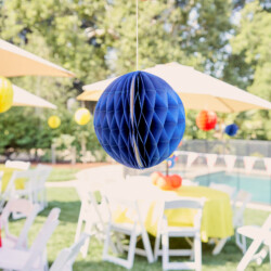 A blue paper ball hanging from the ceiling of an outdoor party.