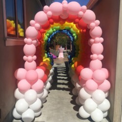 A walkway with balloons and a rainbow arch.