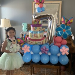 A girl standing next to balloons and cake.