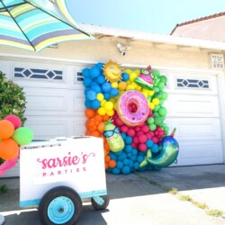 A cart with balloons and an umbrella in front of it.