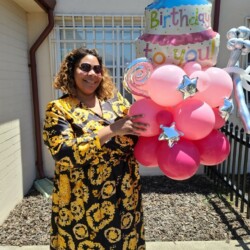 A woman holding balloons in front of a house.