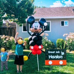A child standing next to balloons in the grass.