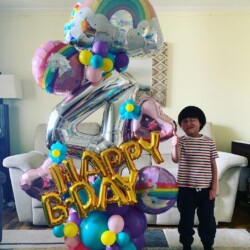A boy standing in front of balloons that say happy birthday