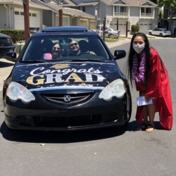 A woman in graduation cap and gown standing next to a car.