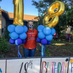 A woman standing next to balloons that are shaped like the number 1 8.