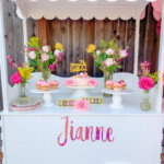 A white booth with flowers and cupcakes on the table.