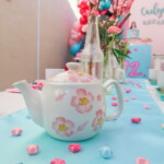 A tea pot on top of a table with flowers.